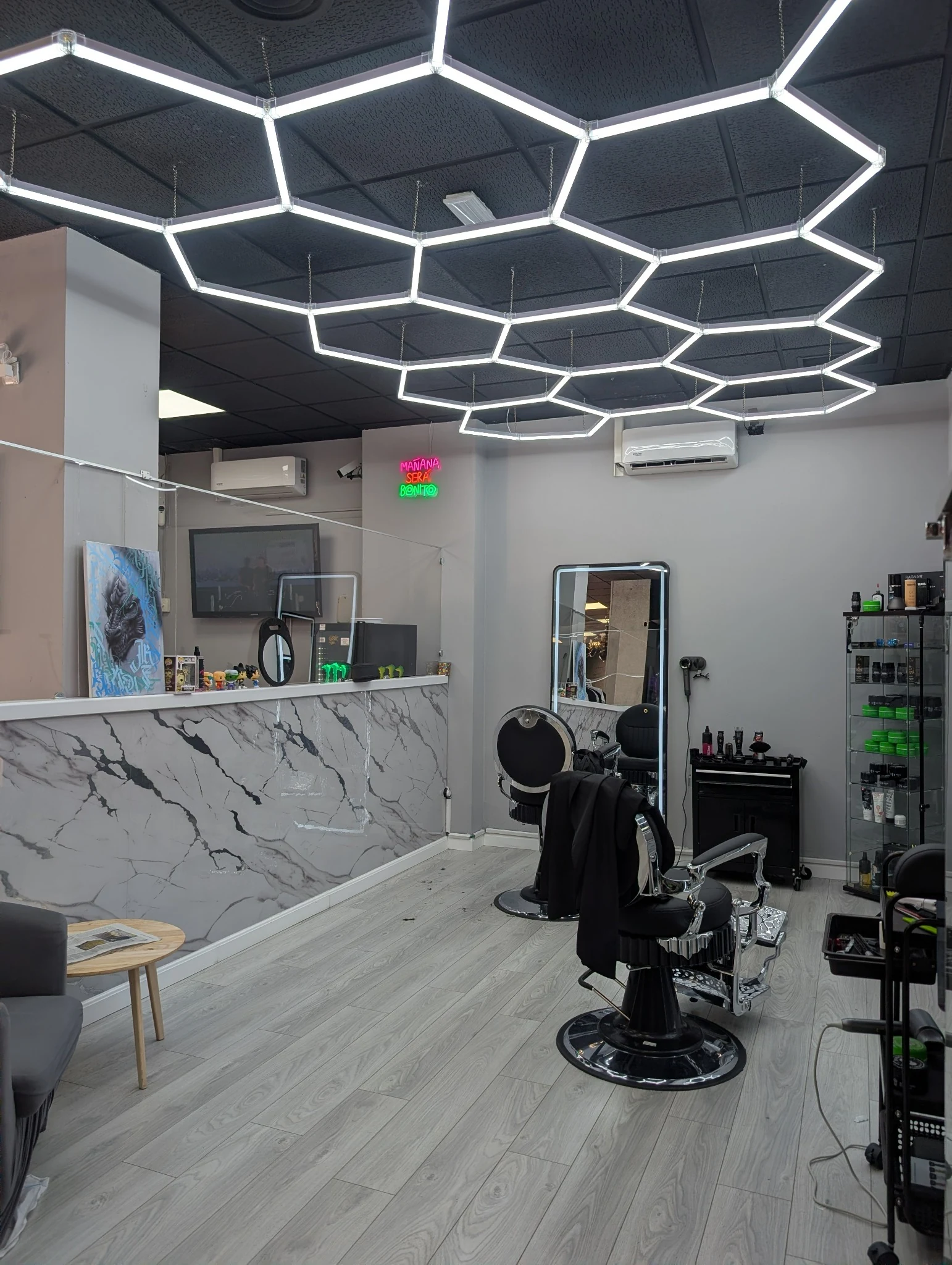 Zona de barbería y recepción con iluminación hexagonal en el estudio.